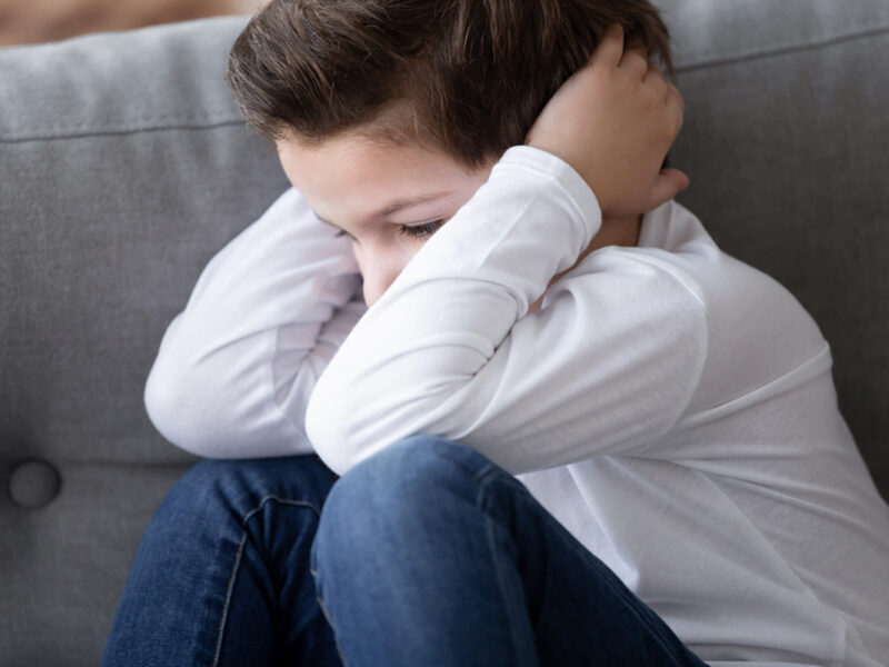Sad stressed stubborn little cute kid boy sit alone hiding feel scared upset lonely abused, preschool child close ears not listening suffer from earache showing rebellious naughty behavior concept