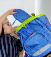 Happy smiling girl preparing for school her backpack. First day of school. Back to school concept. Little child collecting different supplies like pens and books in a bag or satchel