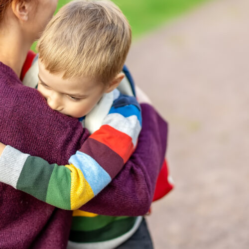 Child with rucksack and with mother in front of a school building. Concept of motherhood and beginning of primary school.
