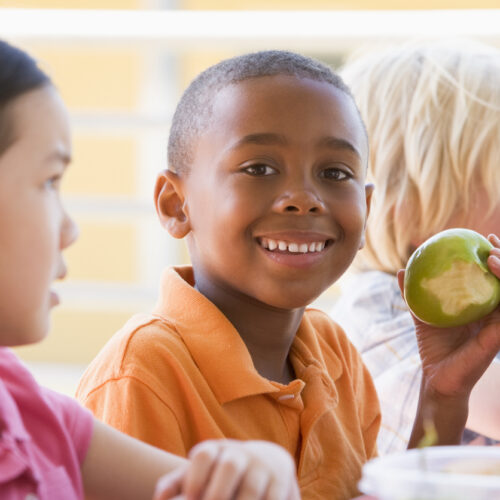 Kindergarten children eating lunch smiling at camera